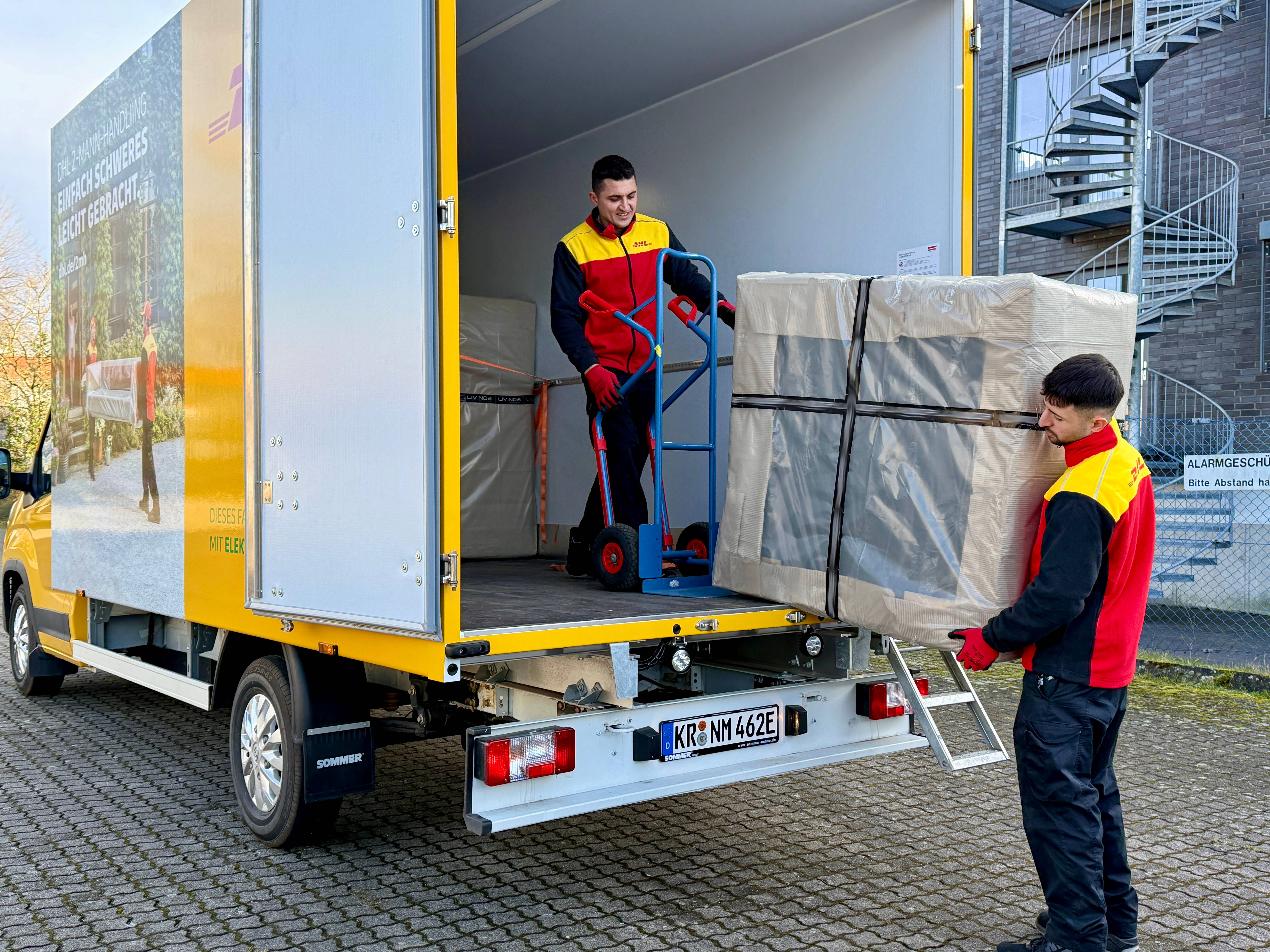 DHL-Mitarbeiter laden eine Sendung aus einem Lieferfahrzeug aus